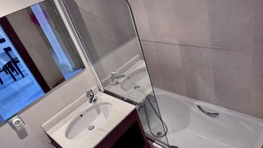 Un baño moderno con un espejo grande, un lavabo y una bañera.