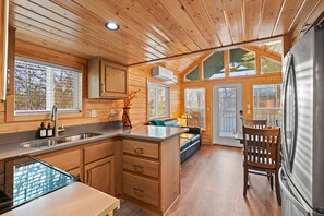 Interior de una cabaña de madera con cocina, comedor y un amplio ventanal.
