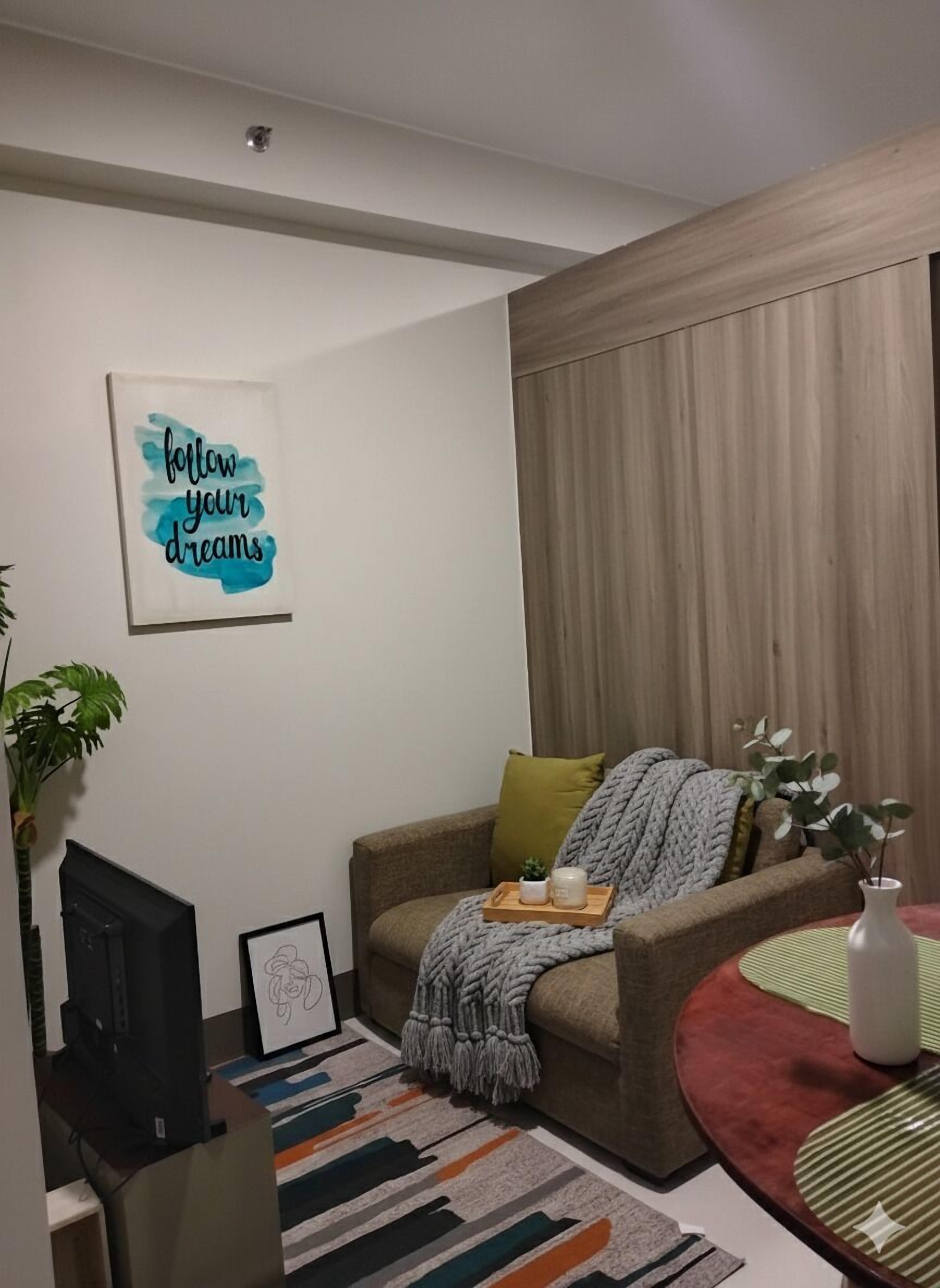 Un salón acogedor con sofá, una mesa de centro, televisor y una obra de arte con un mensaje inspirador.