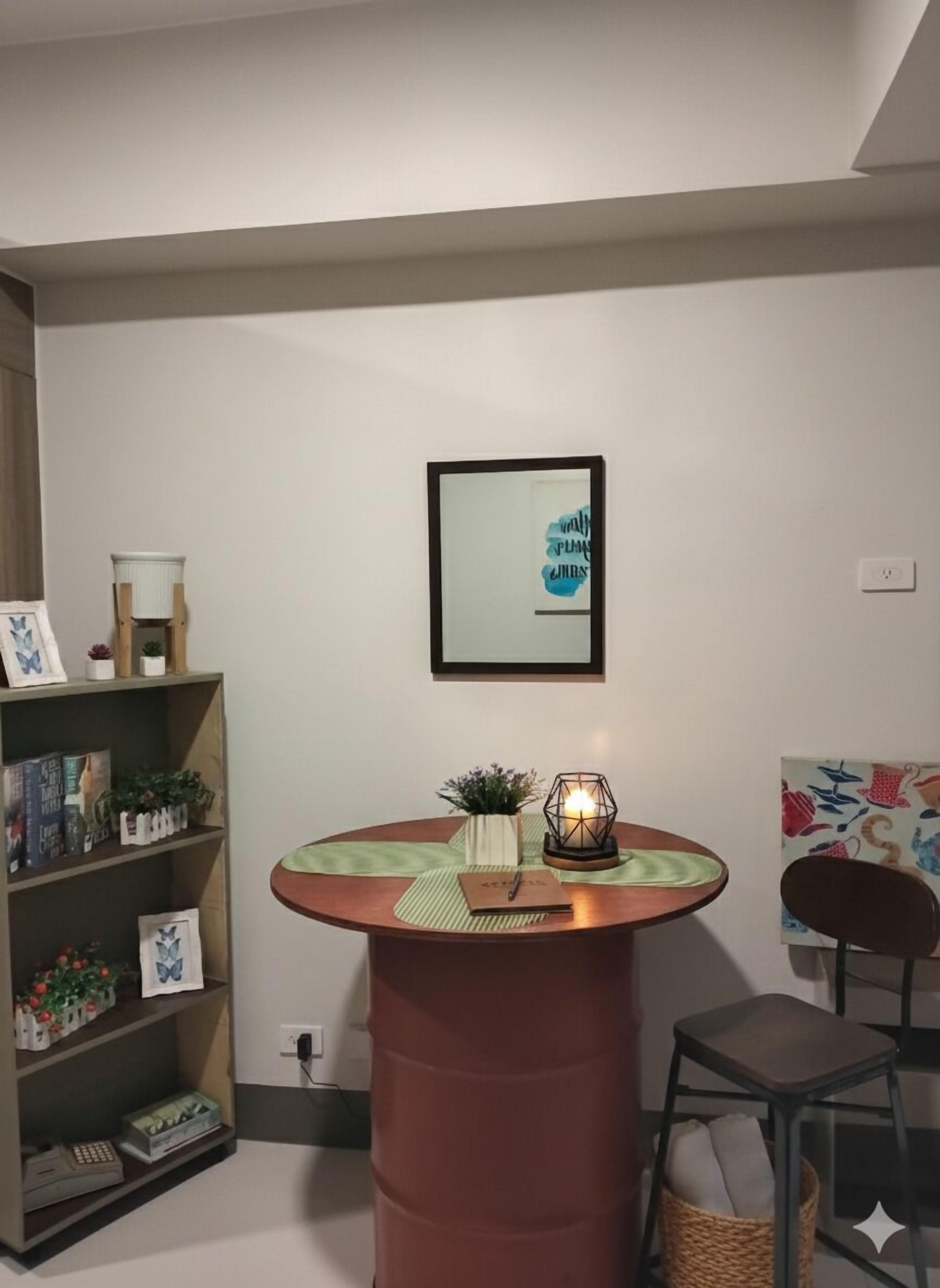A room with a round wooden table, a bookshelf, a framed picture, and a chair.