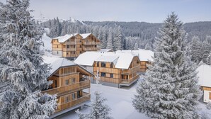 A snow-covered lodge with multiple wooden buildings, surrounded by snow-laden trees and a clear sky.