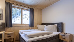 A bedroom with a bed, a nightstand, a wooden dresser, a window with curtains, and a view of a snowy landscape.