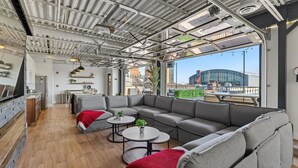 A modern interior with a large gray sectional sofa, round tables, and a kitchen area. - Penthouse of all Penthouses (Indianapolis)