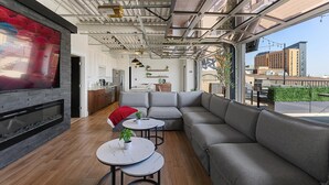 A modern lounge area with a large flat-screen TV, grey sofas, round tables, and a wooden floor. - Penthouse of all Penthouses (Indianapolis)