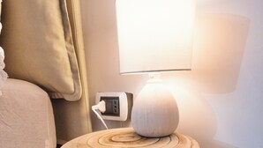 Ett litet sidobord i trä med en lampa, ett eluttag och en kabel.