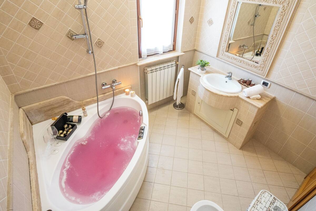 Een badkamer met een badkuip vol roze water, een douche, een wastafel en een spiegel.