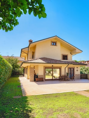 Una casa de dos pisos con un patio, una zona de estar al aire libre techada y un amplio ventanal corredizo.