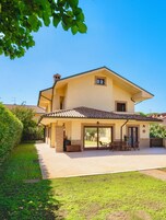 Una casa de dos pisos con un patio, una zona de estar al aire libre techada y un amplio ventanal corredizo.