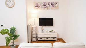 Ett modernt vardagsrum med en vit soffa, en platt-TV som är monterad på väggen, en krukväxt och en väggklocka.