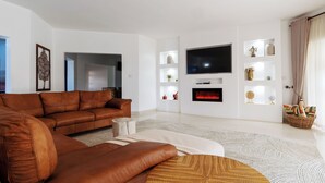 En moderne stue med en brun lædersofa, et fladskærms-tv, en pejs og dekorative reoler.