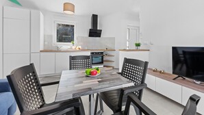 Una cocina moderna con armarios blancos, horno empotrado y comedor con mesa y sillas.