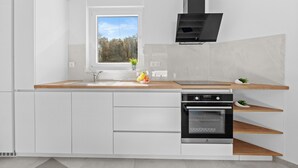 Una cocina moderna con armarios blancos, encimera de madera, horno integrado y ventana con vistas a árboles.