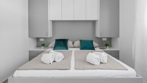 Una habitación de hotel moderna con una cama doble, dos mesitas de noche, un armario empotrado y una pequeña planta en maceta sobre cada mesita.