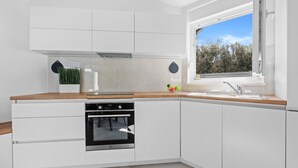 Una cocina moderna con armarios blancos, horno empotrado, encimera de madera y ventana con vistas a árboles.