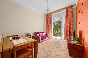A dining area with a wooden table, chairs, a pink sofa, and a view through a glass door. - Seaside Family Apartment Una - Sunny Rab Island (Rab)