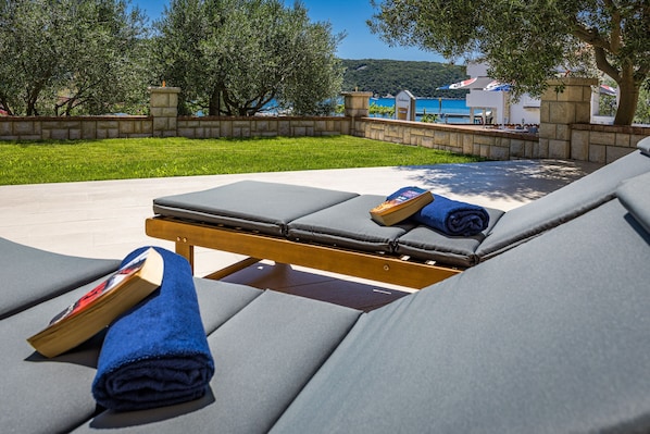 A sunbed with a book and towel, a stone wall, and a view of the sea.