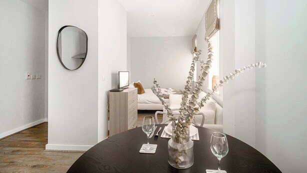 A modern, minimalist bedroom with a dark wooden dining table, a mirror, and a vase with branches. - Modern Studio Apartment in Waterloo, Liverpool (Liverpool)