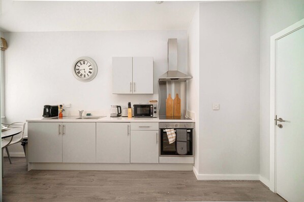 A modern kitchen with white cabinets, a microwave, a coffee maker, and a clock on the wall. - Modern Studio Apartment in Waterloo, Liverpool (Liverpool)