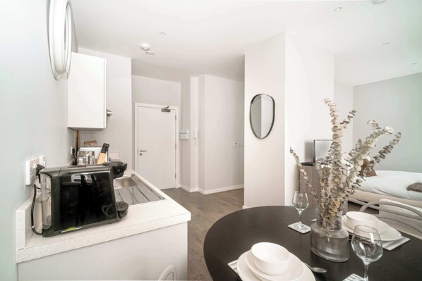 A modern kitchen with a toaster, a sink, and a dining area with a table set for two. - Modern Studio Apartment in Waterloo, Liverpool (Liverpool)