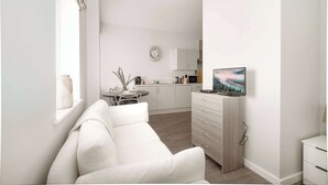 A modern, minimalist living room with a white sofa, a small dining table, and a kitchen area in the background. - Modern Studio Apartment in Waterloo, Liverpool (Liverpool)