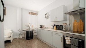 A modern kitchen with white cabinets, a stainless steel range hood, and a dining area with a round table and chairs. - Modern Studio Apartment in Waterloo, Liverpool (Liverpool)