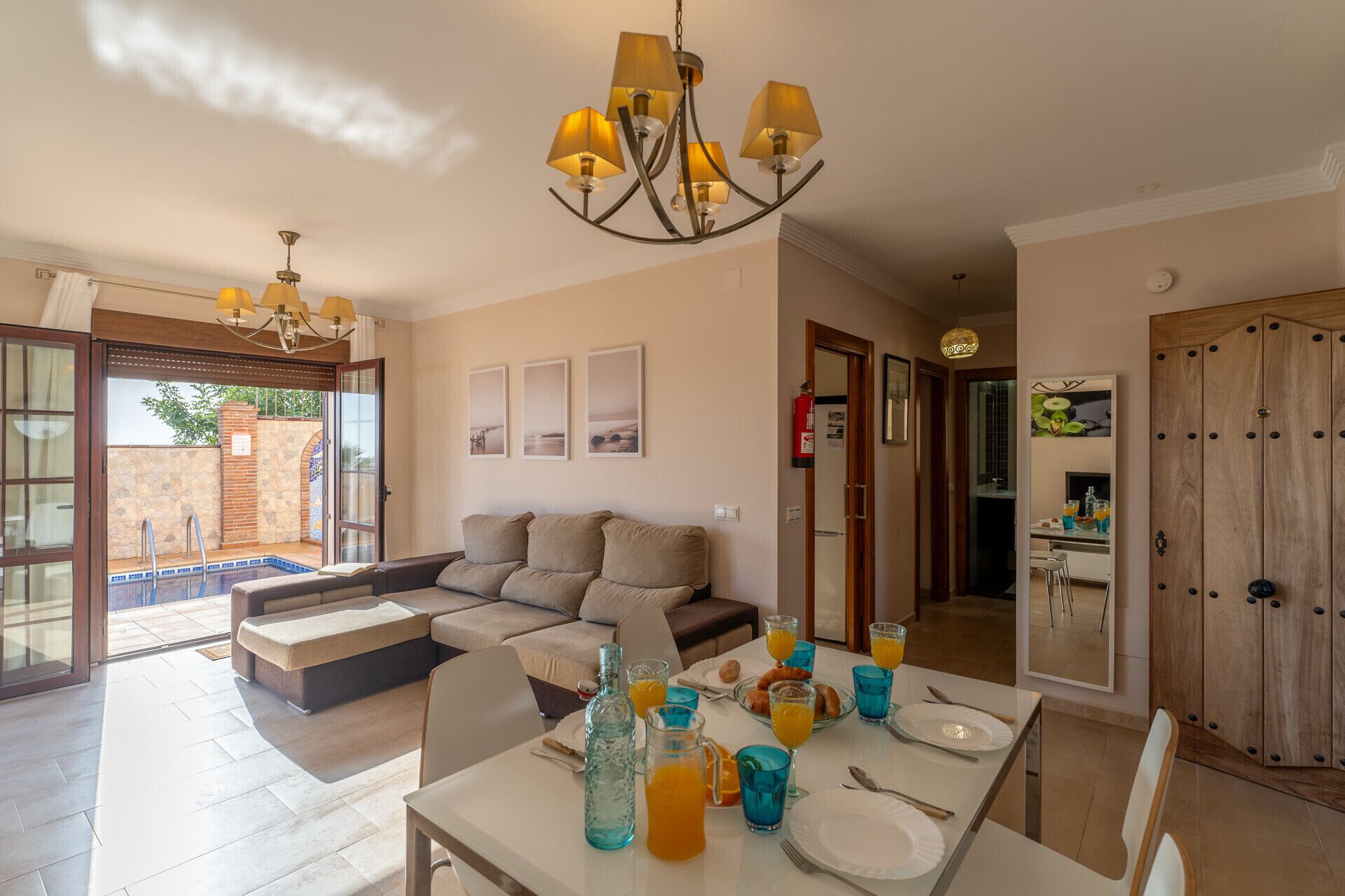 A spacious living area with a sofa, dining table set for breakfast, and a view of the outdoor pool.