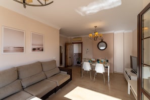 A living room with a sofa, dining table with chairs, a clock, and a TV. - Villa Miguel Franco (Nerja)