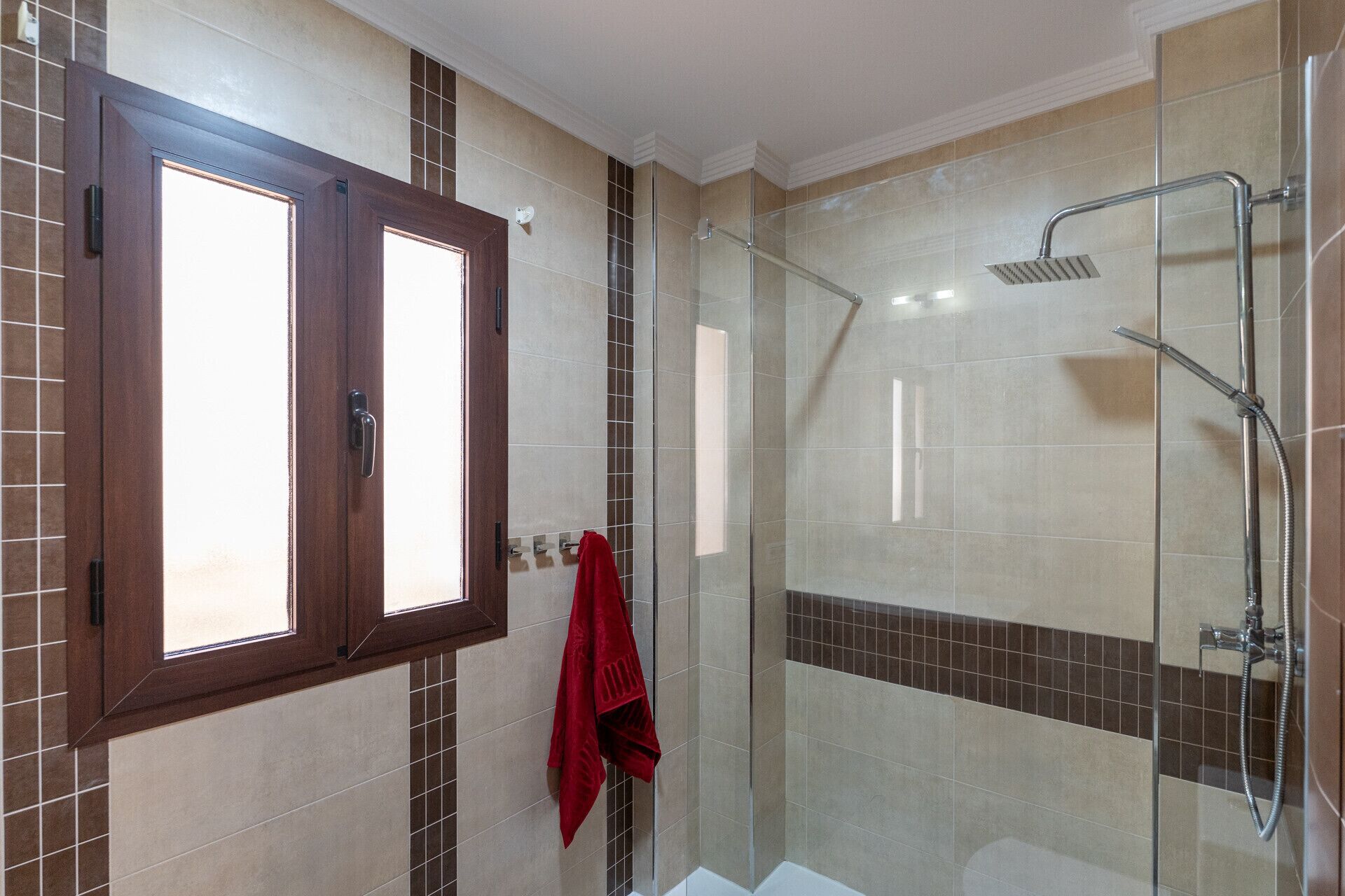 Une salle de bain avec une douche à parois de verre, une baignoire et une fenêtre avec un cadre en bois.