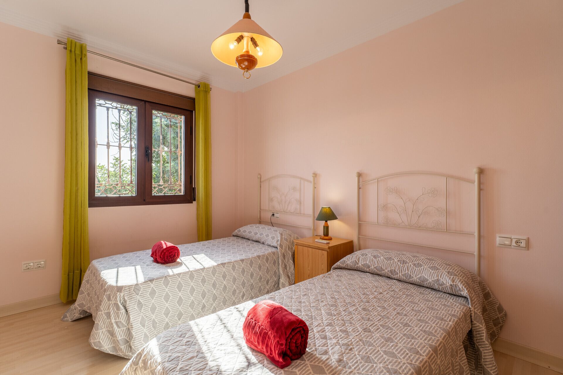 Een slaapkamer met twee bedden, een raam met gele gordijnen en een hanglamp.