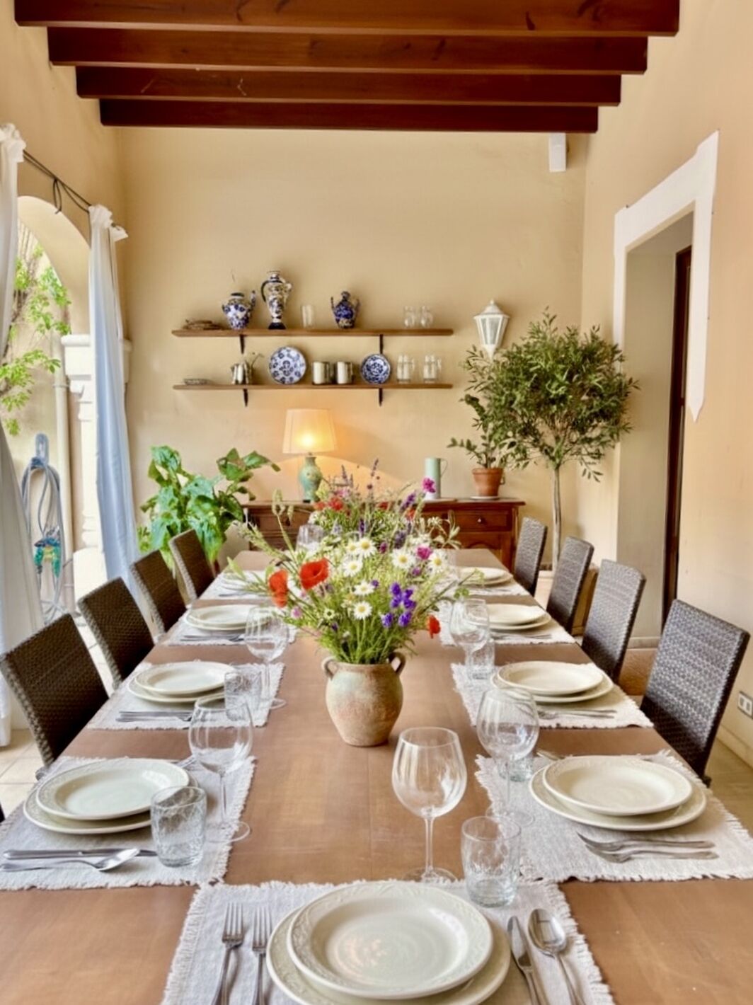Un coin repas avec une longue table dressée pour le repas, entourée de chaises, et un vase de fleurs placé au centre.