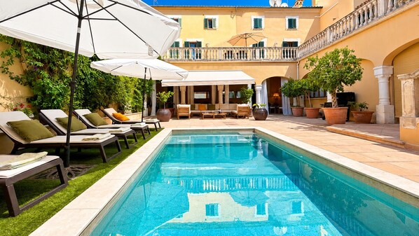 Ein Poolbereich mit Liegestühlen, Sonnenschirmen und Pflanzen in Töpfen.