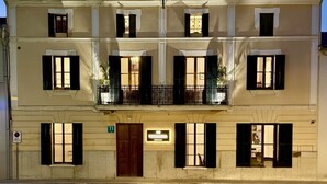 A multi-story building with a symmetrical facade, large windows with shutters, and a balcony with a railing.