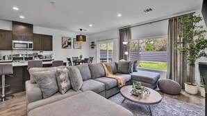 Een moderne woonkamer met een grijze modulaire bank, een ronde salontafel, en een eethoek met een keuken op de achtergrond.