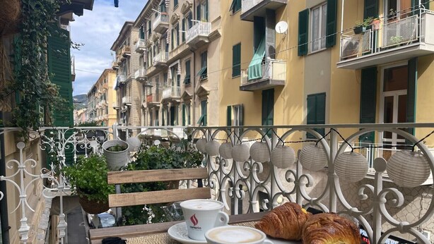 A balcony with a table set for two, featuring a croissant and two cups of coffee.