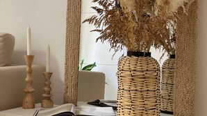 A room with a white sofa, a mirror reflecting a plant, and a table with candles and a book.