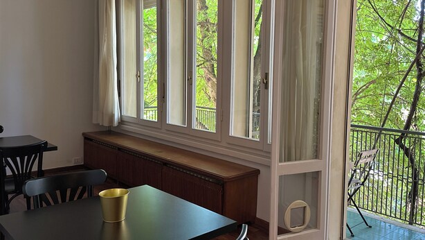 A room with a dining table, chairs, a bench, and a window with a view of greenery. - Room & Breakfast D'Annunzio (Ravenna)