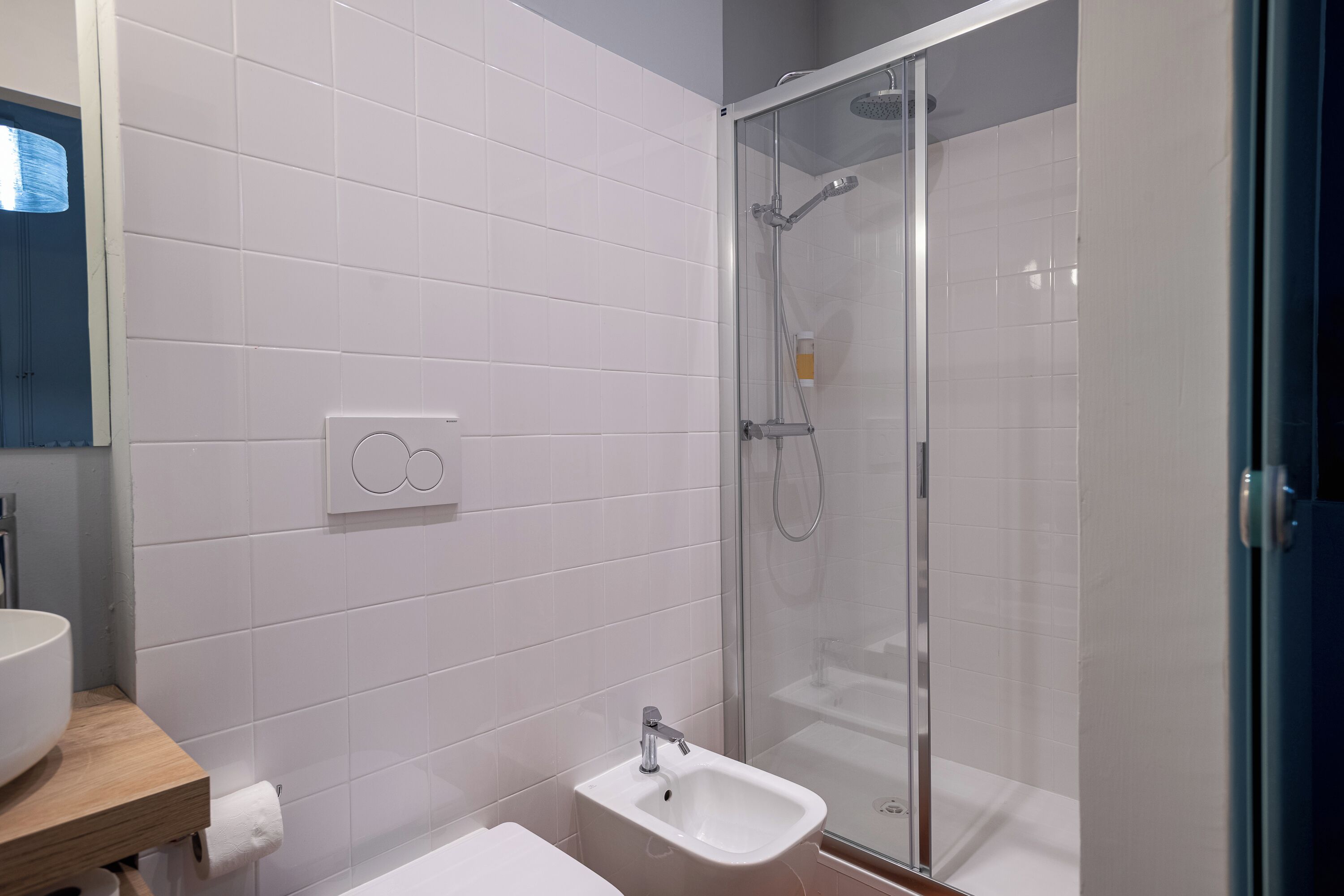 A modern bathroom with white tiles, a glass-enclosed shower, a sink, and a toilet.