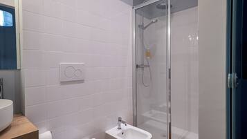 A modern bathroom with white tiles, a glass-enclosed shower, a sink, and a toilet.