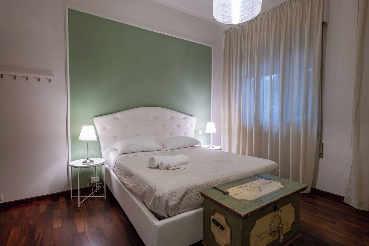A neatly arranged bedroom with a bed, bedside lamps, a small table, and a window with curtains.