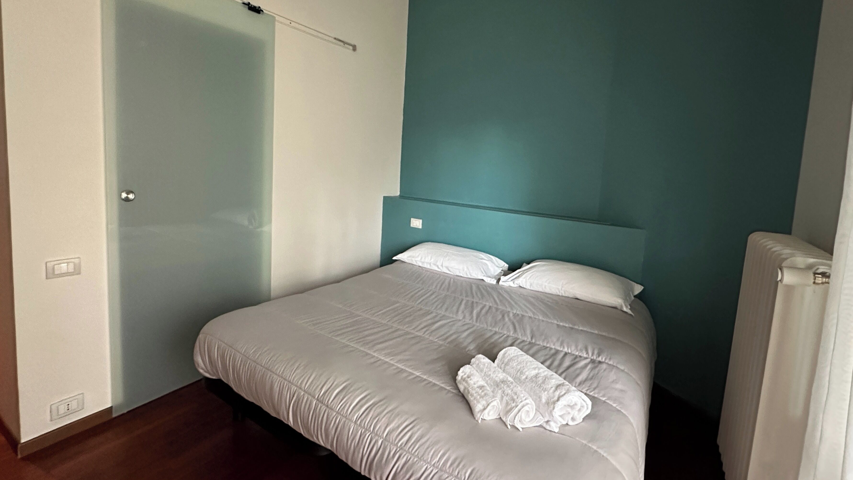 A bedroom with a bed, white bedding, and a teal accent wall.