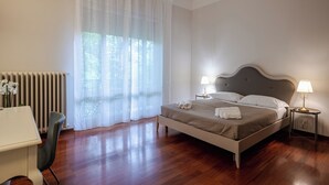 A bedroom with a bed, bedside lamps, a radiator, a chair, and a window with sheer curtains. - Room & Breakfast D'Annunzio (Ravenna)