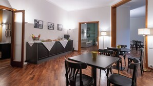 A dining area with a wooden table and chairs, a kitchen area with a counter and appliances, and a living space with a sofa and a lamp. - Room & Breakfast D'Annunzio (Ravenna)