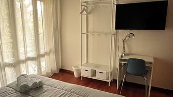 A bedroom with a bed, a desk, a chair, a wardrobe, and a TV mounted on the wall.