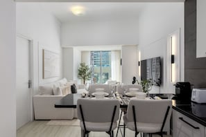 A modern kitchen with a dining area, white furniture, and a large window.