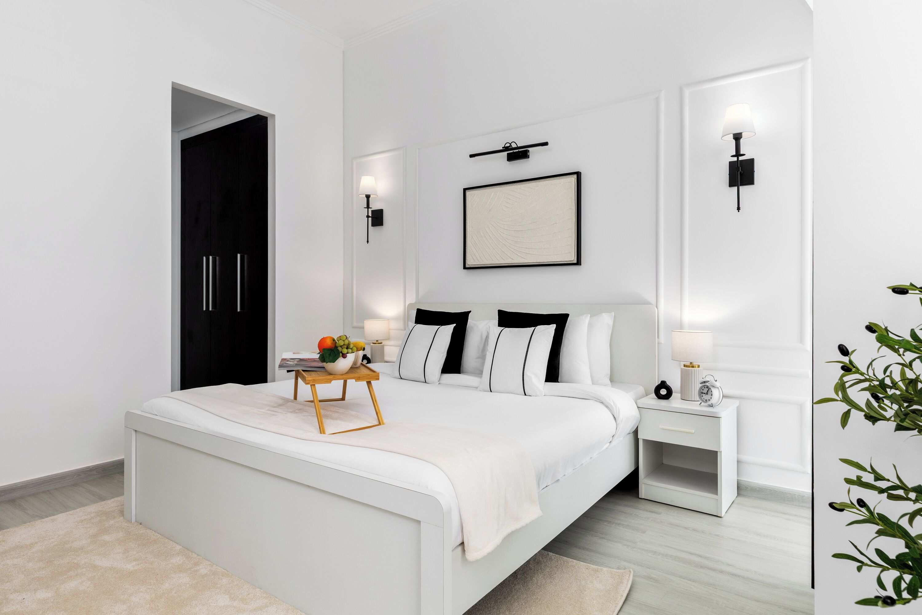 A modern bedroom with a large bed, bedside tables, a framed picture on the wall, and a door to the left.