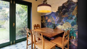 A dining area with a wooden table and chairs, a large painting on the wall, and a hanging light fixture.