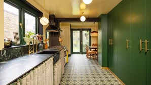 A kitchen with a marble countertop, a sink, and a stove. There is a dining area with a table and chairs. The walls are green, and there are hanging lights.