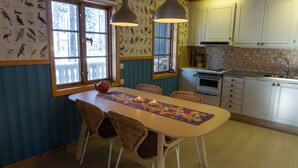 Une cuisine équipée d’une table à manger, de chaises, d’une cuisinière et d’une fenêtre donnant sur des arbres.