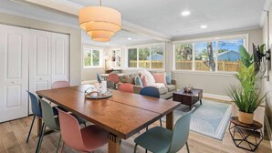 Un comedor con una mesa de madera, sillas coloridas, una lámpara colgante y vistas al patio trasero a través de amplios ventanales.