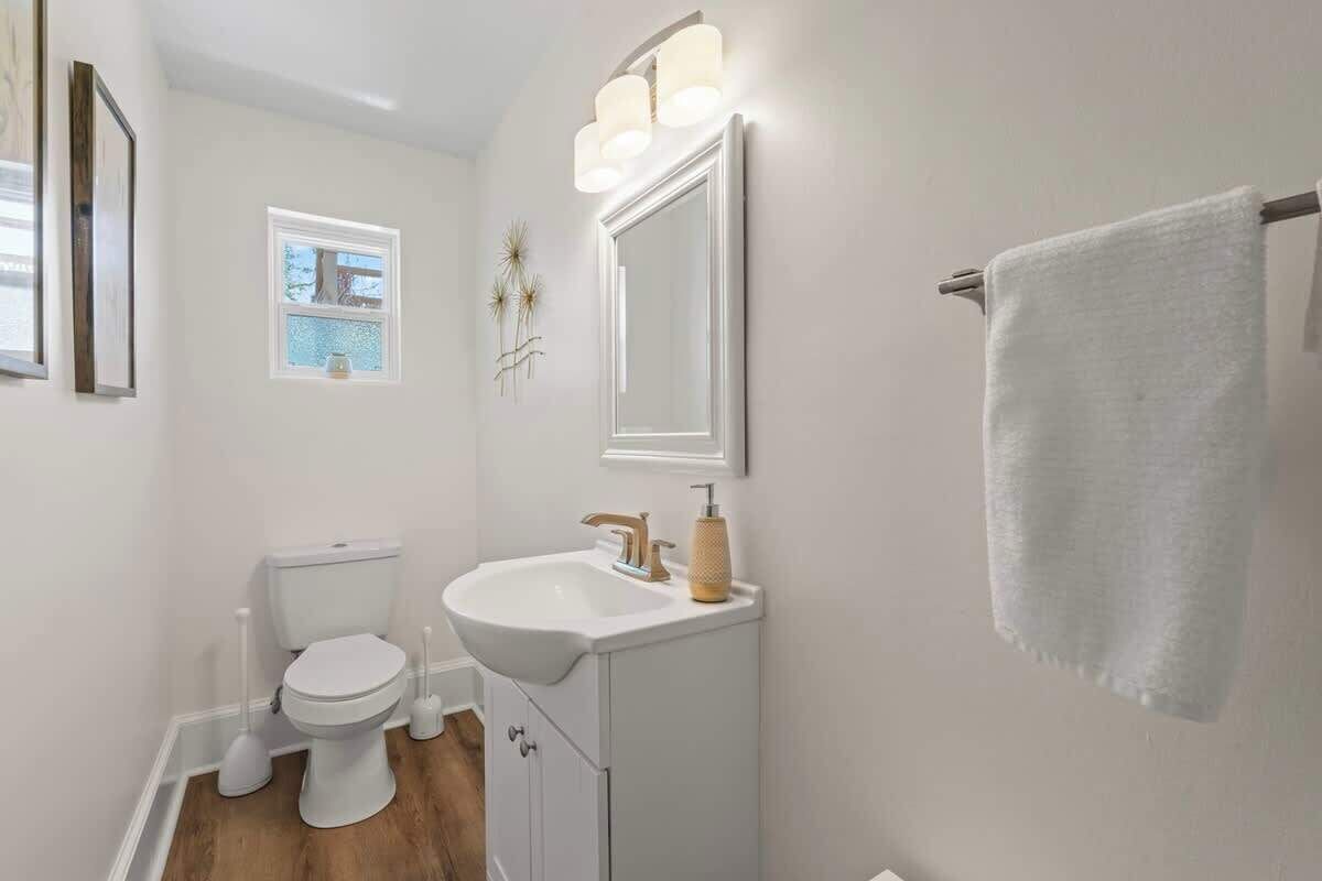 Un baño con inodoro, lavamanos, espejo y perchero para toallas.